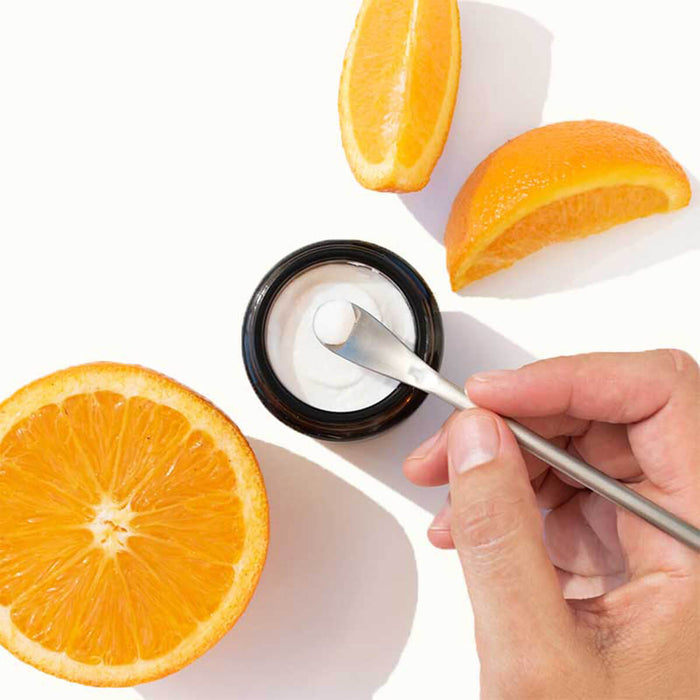 Hand scooping Solid Toothpaste Orange with Fluoride from a jar, surrounded by orange slices on a white background