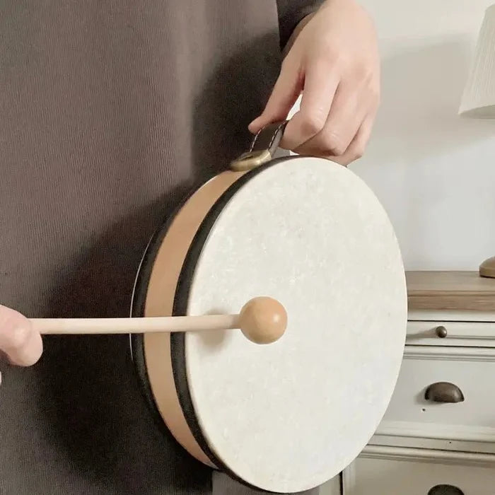 Person playing a small drum with a wooden stick in a room setting.