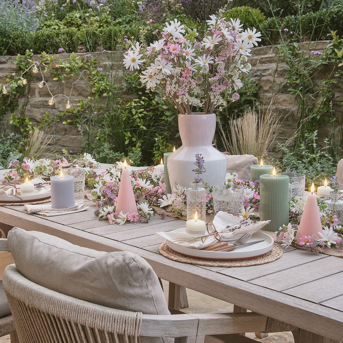 Outdoor dining table with LED candles, a vase of flowers, and flower garlands and wreaths