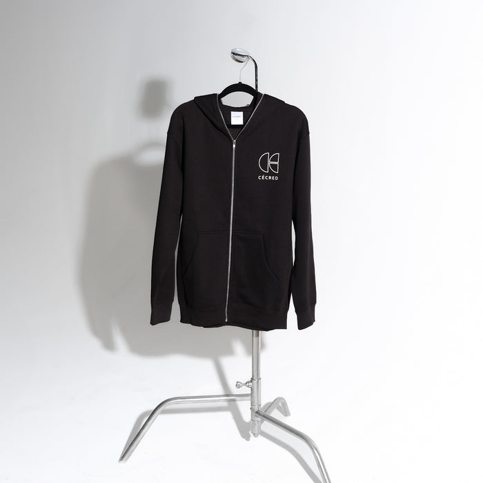 Cécred black zip-up hoodie displayed on a standing chrome garment rack against a soft white background, showcasing the full silhouette and front zip detail