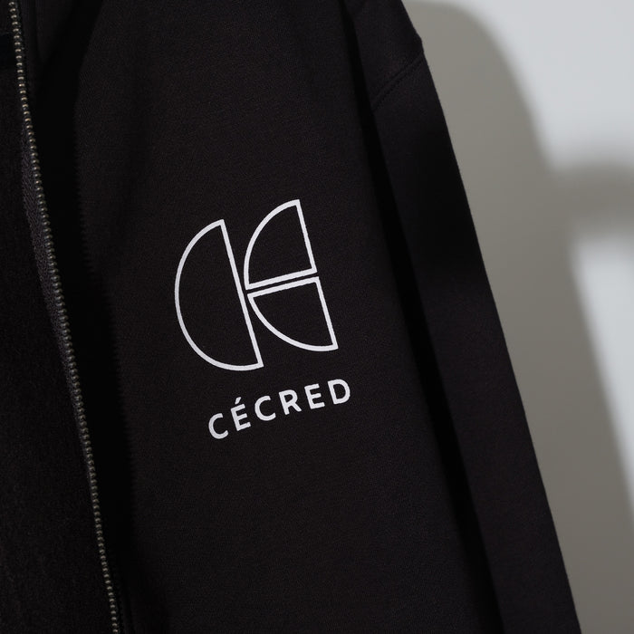 Close-up of the Cécred monogram logo and wordmark embroidered on the chest of the black zip-up hoodie