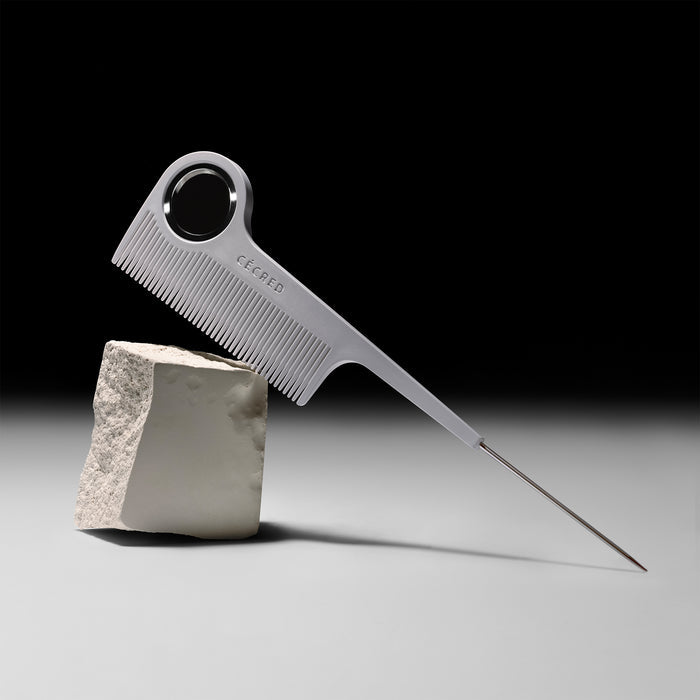 Cécred rat tail comb with metal tail balanced horizontally on angled rock.