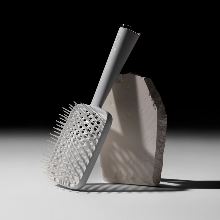 Cécred paddle vent brush leaning against textured stone on gradient background.