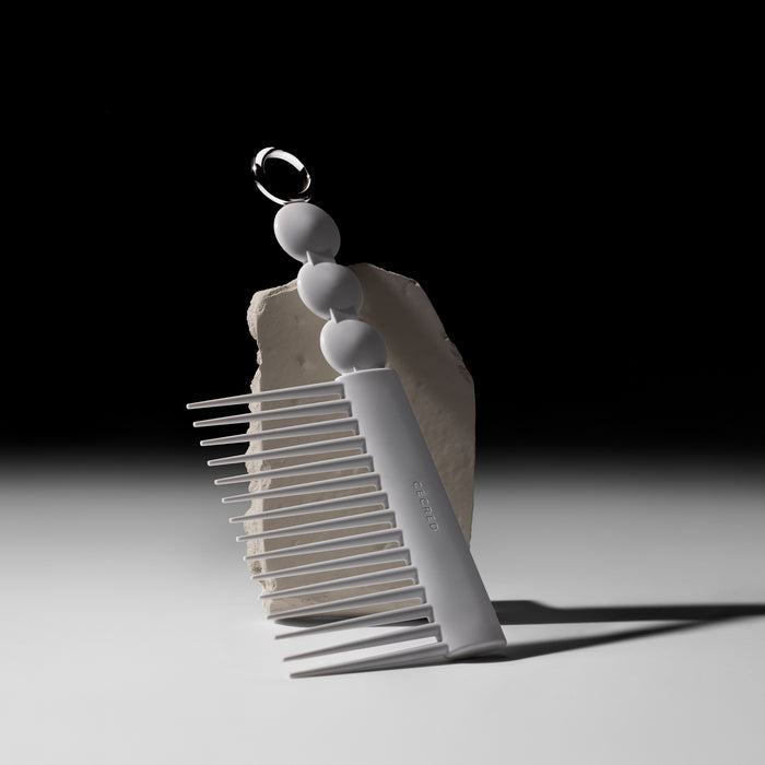 Cécred rake comb with sculptural handle and wide-set teeth, propped against a textured stone on a gradient background.