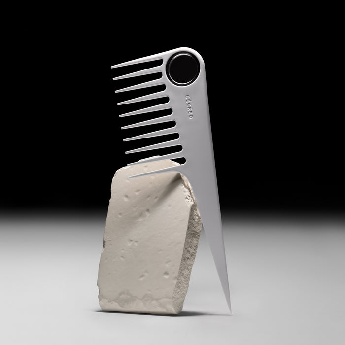 Cécred wide-tooth comb with spherical handle balancing on a block of stone.