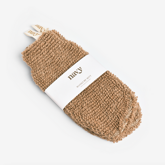 A beige manicure mitt made from hemp fibers, displayed with its packaging which has a brand label on it. exfoliate and pamper your hands