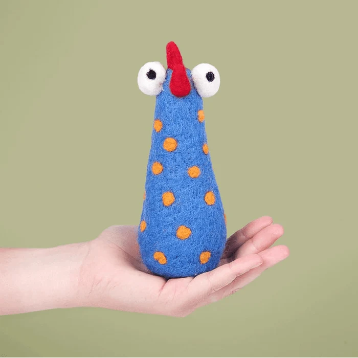 Felted blue chicken toy with orange spots held in a hand against a green background