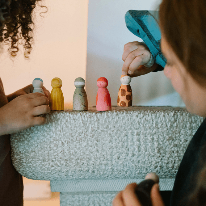 Two children playing with colorful peg people on furniture