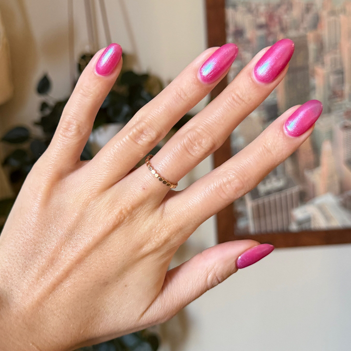 Hand with almond-shaped nails coated in HARD LAUNCH pinky-purple iridescent duochrome polish indoors background