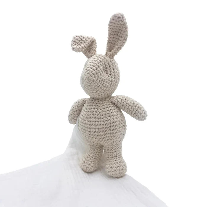 Crocheted bunny toy holding a white blanket on a white background
