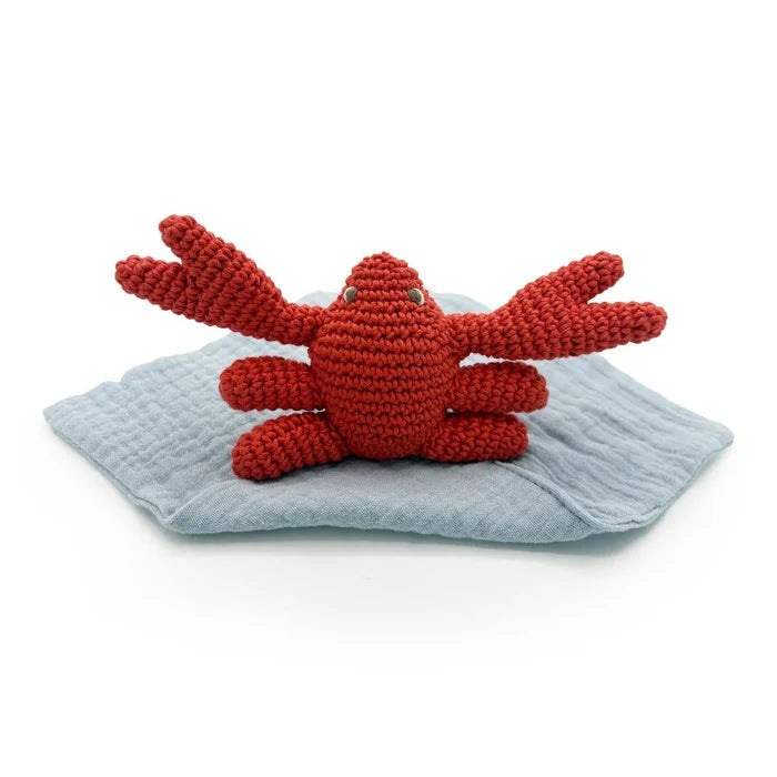 Red crocheted crab toy on a grey blanket with a white background