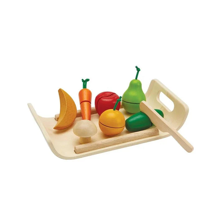 Colorful toy fruits and vegetables on a wooden tray with a knife on a white background