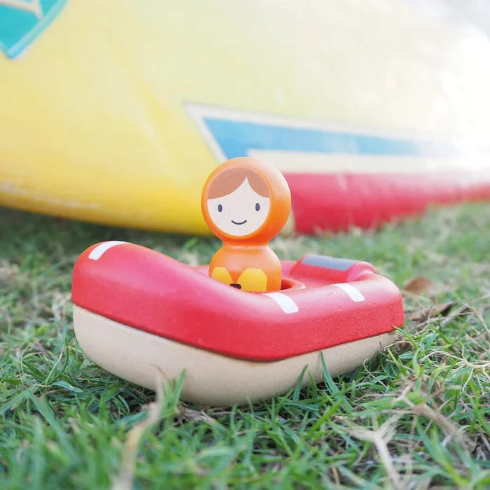 Small figurine in a red and white lifeboat on grass with colorful boats in the background