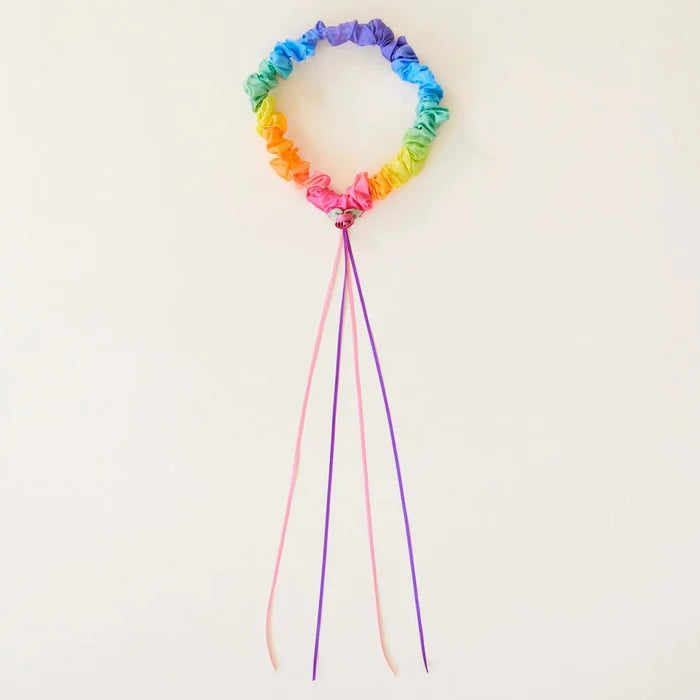 Rainbow colored garland with pink and purple ribbons attached on a light background