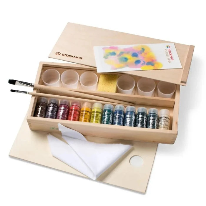 Wooden art supply set with paint bottles, brushes, and a towel on a white background