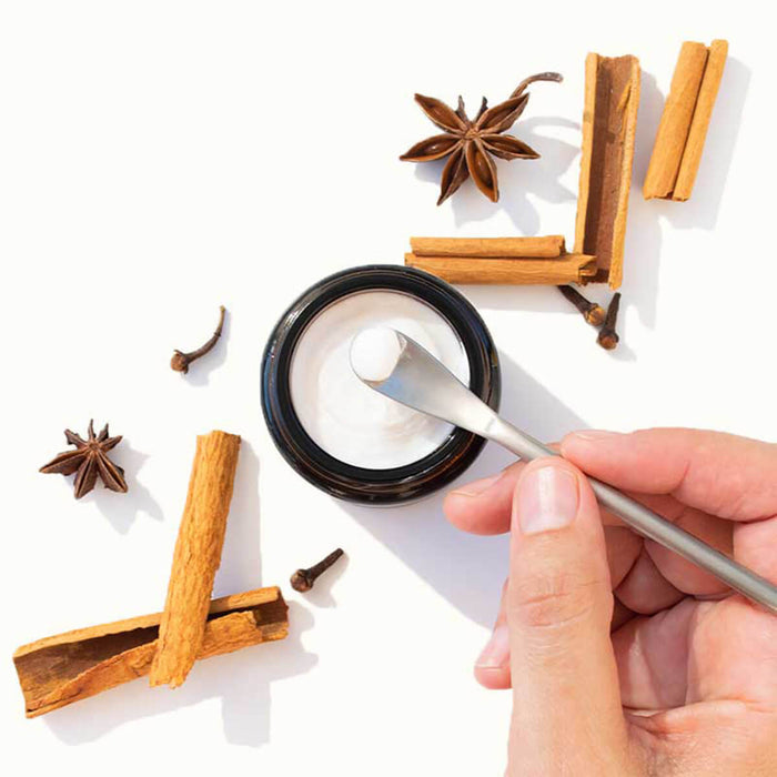 Hand scooping Solid Toothpaste Cinnamon with Fluoride from a jar, surrounded by cinnamon sticks and star anise on a white background