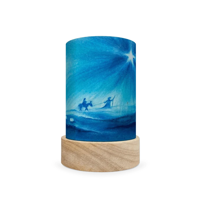 Decorative lamp with scene of Mary and Joseph following a star on a wooden base on a white background